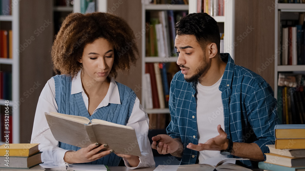 Students studying in library doing homework preparing for exam young girl reads textbook searches information in book helping friend with education guy writes notes in notebook friends talk discuss