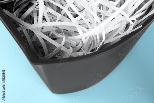 Shredded paper strips in trash bin on light blue background  closeup