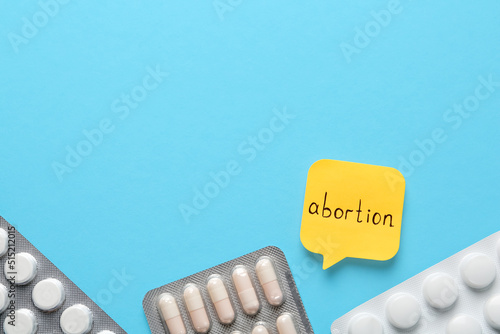 Paper note with word Abortion and pills on light blue background, flat lay. Space for text