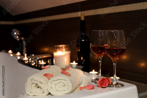 Glasses of wine, towels and rose on tub in bathroom. Romantic atmosphere