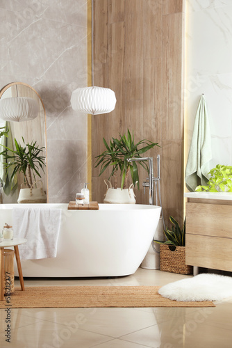 Modern white tub and beautiful green houseplants in bathroom. Interior design