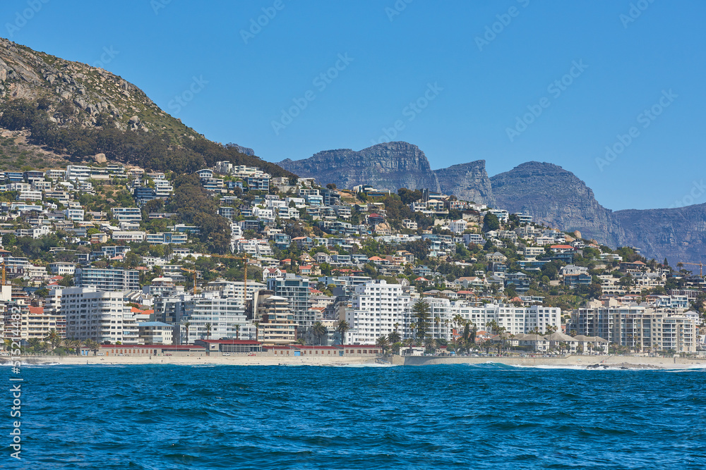Panorama seascape with clouds, blue sky, and fancy hotel apartment buildings in the background. Sea Point with the Twelve Apostles and Table Mountain National Park in Cape Town, South Africa