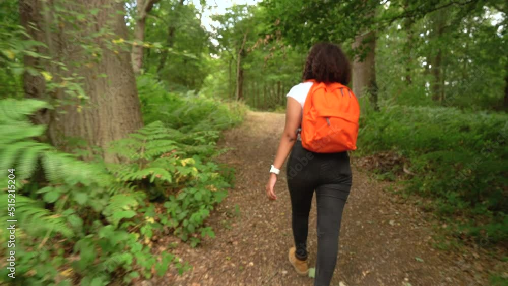 Teenage mixed race African American girl young woman hiking with orange backpack in forest woodland Teenage mixed race African American girl young woman hiking with orange backpack in forest woodland