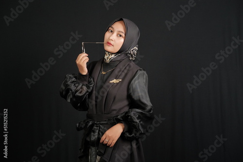 Portrait of Asian Muslim woman wearing hijab holding glasses, isolated on black background