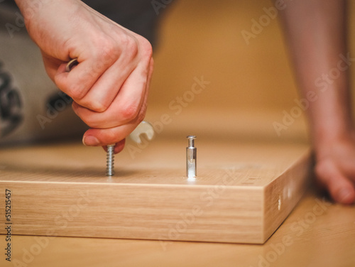The hands of a Caucasian young man twist a bolt on the wooden part of the bed