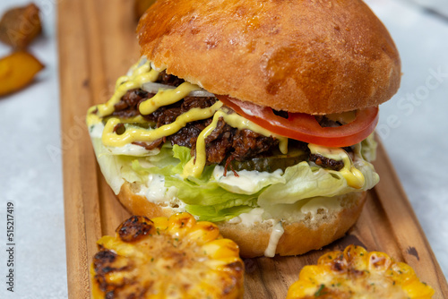 Juicy beef burger on a wooden board with fried corn close up