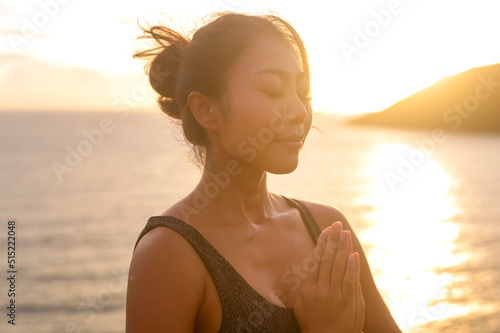 Young asian woman in sportswear doing yoga on the rock at seaside during Sunset, health and meditation concept