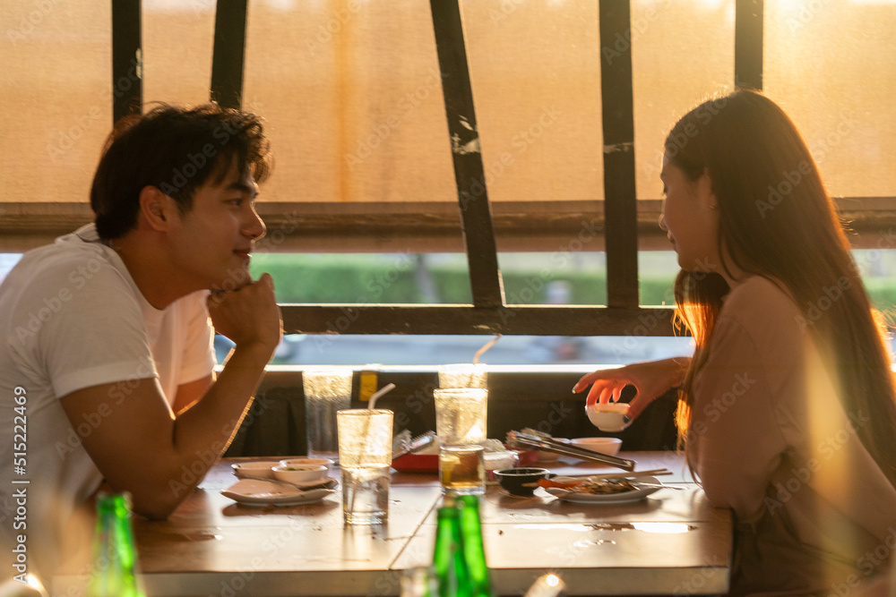 young woman and an Asian man sitting and eating grilled pork or Sukiyaki and Shabu using a Korean stove have dinner together at a Korean-style Shabu restaurant. young woman and an Asian man sitting and eating grilled pork or Sukiyaki and Shabu using a Korean stove have dinner together at a Korean-style Shabu restaurant.