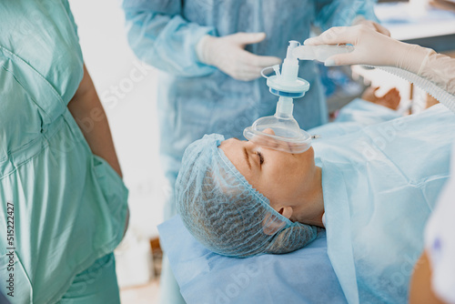 Close up hands of doctor anesthesiologist holding breathing mask on patient face during operation photo