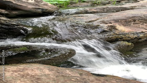 Mountain river - a small waterfall on a river with crystal clear water that flows among gray stones in a green forest on a cloudy summer day. Big stones near the pond