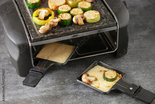Delicious traditional Swiss melted raclette cheese on diced boiled or baked vegetables served in individual skillets