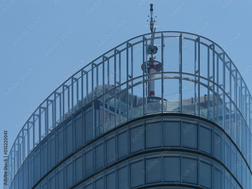 Close-up view of the top of a modern business tower with windows and a clear blue sky in the background Close-up view of the top of a modern business tower with windows and a clear blue sky in the background