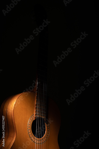 Classical guitar dramatically lit from above on a black background.  