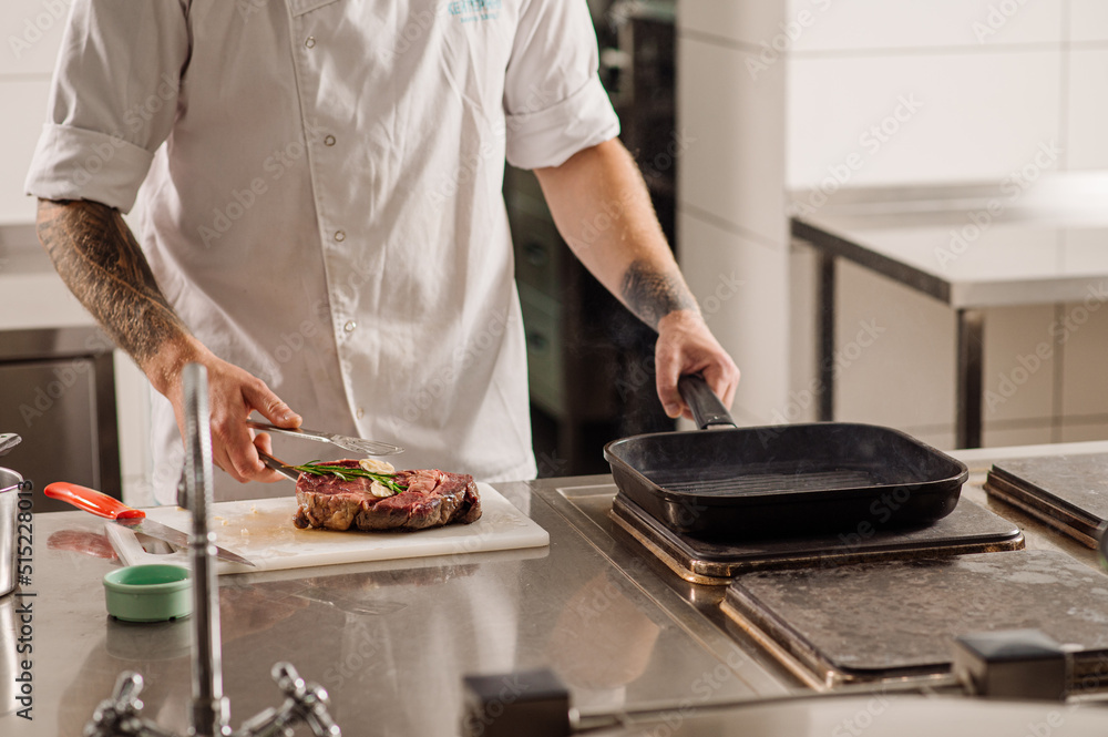 Chef is friing a steak in the pan at the restaurant kitchen
