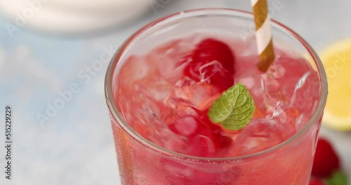 Spring or summer refreshing cold cocktail or mocktail with berries and lemon, raspberry lemonade being stirred with a straw