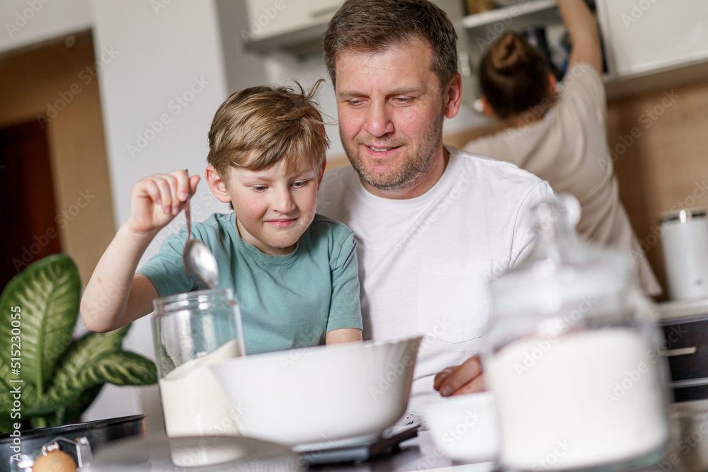 Dad and little son baking together in kitchen, preparing dough for pie, having fun at home, preparing a surprise for mom on mother's day Dad and little son baking together in kitchen, preparing dough for pie, having fun at home, preparing a surprise for mom on mother's day