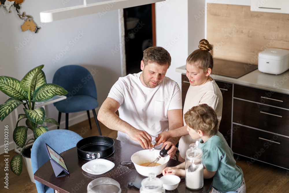 Dad and little daughter and son baking together in kitchen, preparing dough for pie, having fun at home during quarantine Dad and little daughter and son baking together in kitchen, preparing dough for pie, having fun at home during quarantine