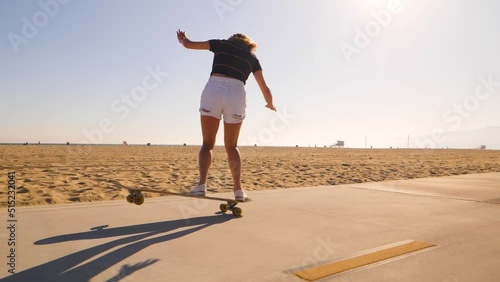 Rear View Of A Sporty Woman Riding Skateboard In Skatepark On Desert Landscape - wide, slow motion photo