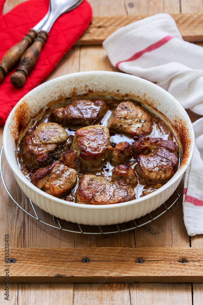 Tenderloin baked in onion sauce with herbs on a wooden table. Rustic style.