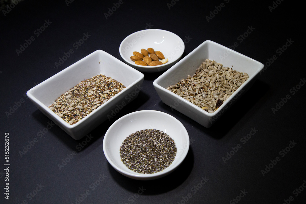 Almonds, chia and other healthy vegan seeds in white porcelain bowls on a black background Almonds, chia and other healthy vegan seeds in white porcelain bowls on a black background