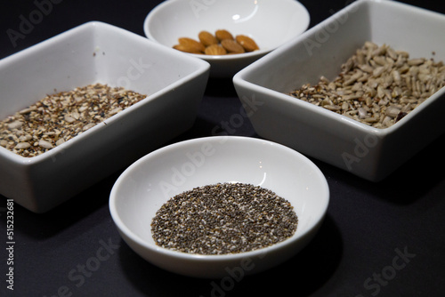 Almonds, chia and other healthy vegan seeds in white porcelain bowls on a black background