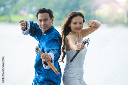 A couple of Young man and woman practicing Kung Fu or Martial art with Nunchaku for fighting competition in the park. photo
