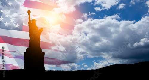 Statue of Liberty with a large american flag and blue sky on background.