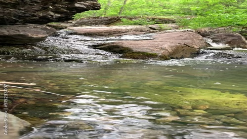 Mountain river - a small waterfall on a river with crystal clear water that flows among gray stones in a green forest on a cloudy summer day. Close up of a rock next to a body of water