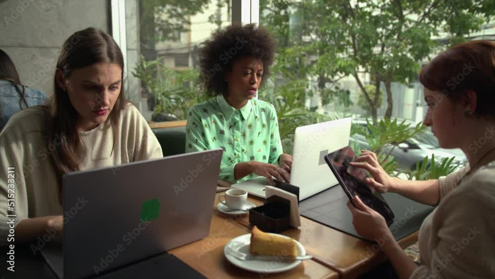 Group of female colleagues working at cafe in front of laptops and tablet. Diverse millenial women working remotely Group of female colleagues working at cafe in front of laptops and tablet. Diverse millenial women working remotely