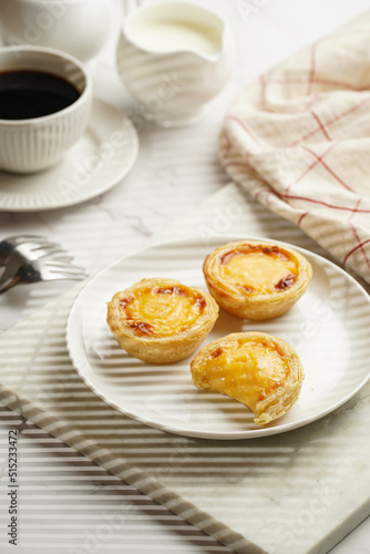Traditional portuguese vanilla pudding puff pastry pastel de nata on white plate on marble board with a cup of coffee in white porcelain