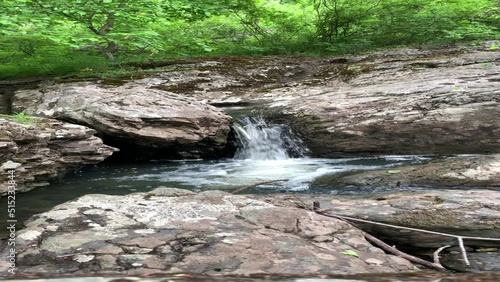 Pure mountain stream - a waterfall flows in the middle of a green forest, between huge boulders. Moss-covered gray boulder stones