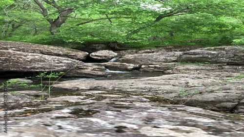 Pure mountain stream - a waterfall flows in the middle of a green forest, between huge boulders. Moss-covered gray boulder stones