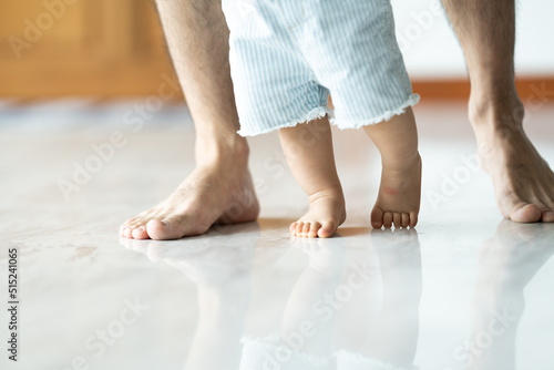 Baby learning to walk with father helping him learn at home by holding hand