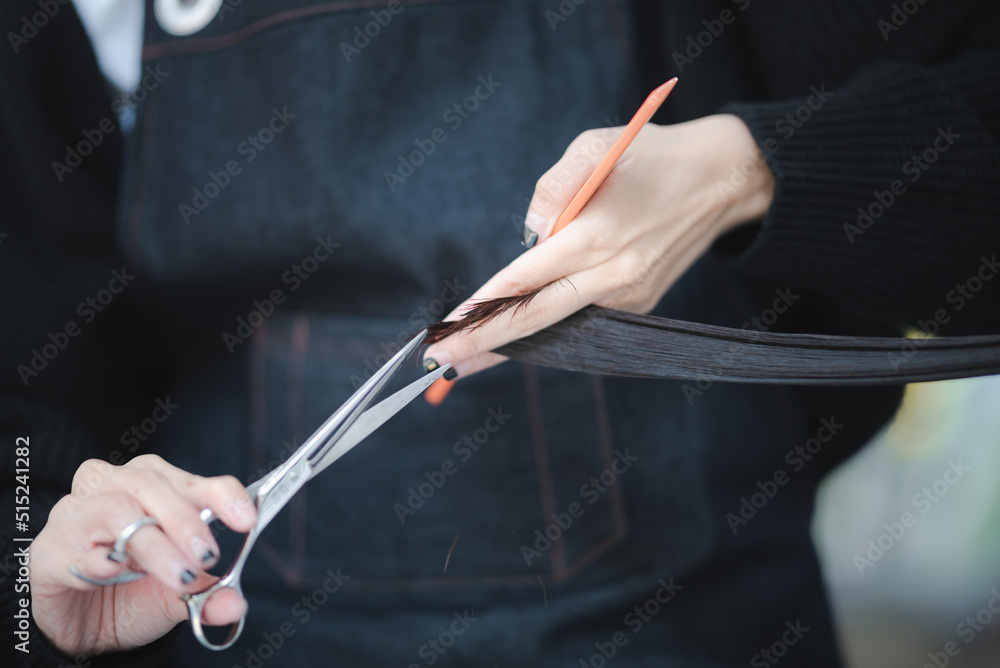 Closeup of hands of male hair stylist holding comb and scissor cutting and trimming hair of female customer