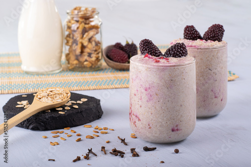 Overnight oats with blackberry fruits, a tablespoon of oats to the right, and in the background milk and nuts.