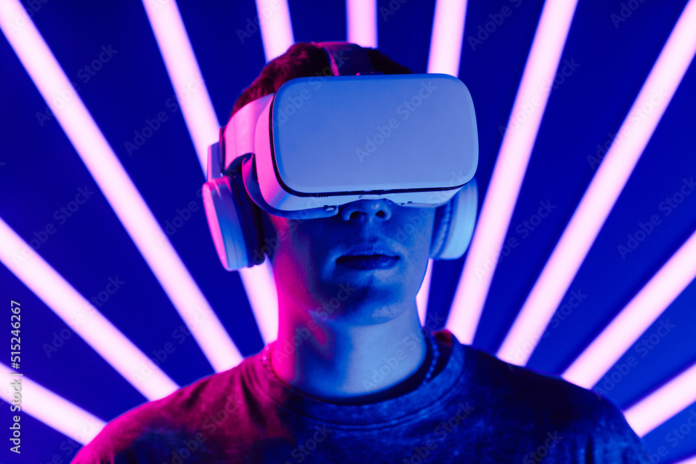 Futuristic shot of young man wearing VR headset with neon light beams in background, copy space Futuristic shot of young man wearing VR headset with neon light beams in background, copy space