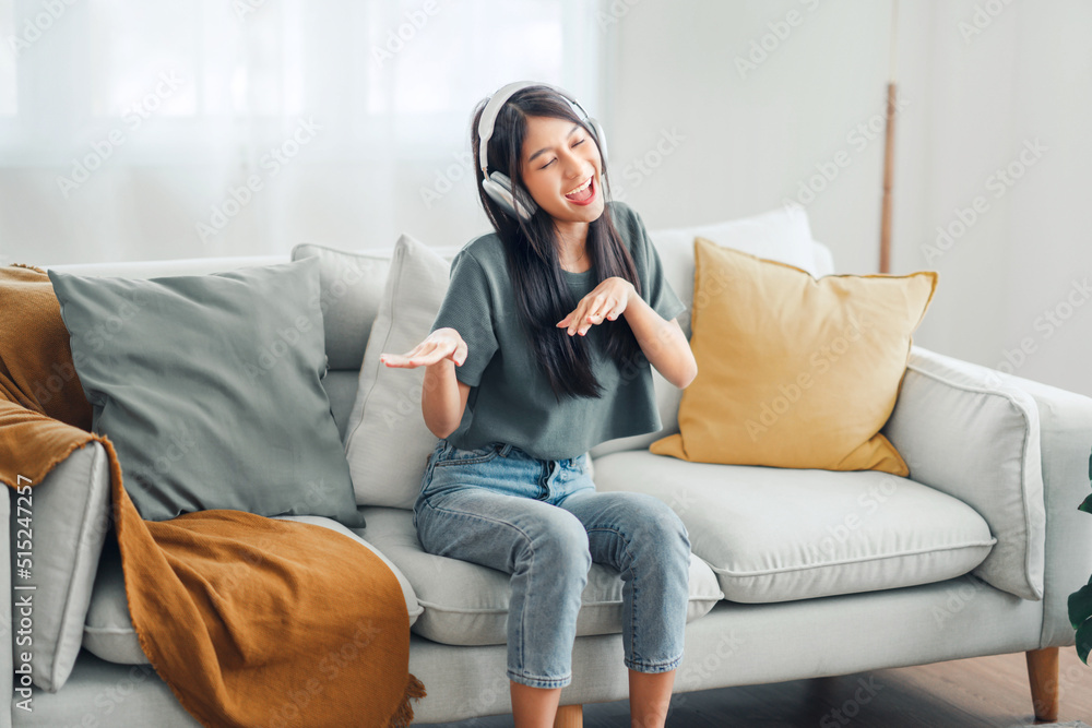 Happy carefree asian woman wearing headphones have fun moving listening to music relax in living room, She dance enjoy leisure weekend at home. Happy carefree asian woman wearing headphones have fun moving listening to music relax in living room, She dance enjoy leisure weekend at home.