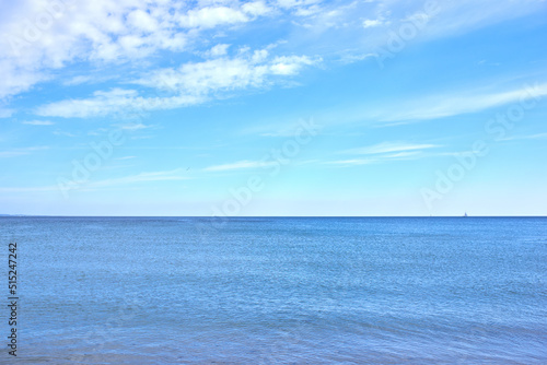 Copy space at sea with a cloudy blue sky background. Calm ocean waves at an empty beach with a sailboat cruising in the horizon. Scenic and picturesque landscape view for a peaceful summer holiday