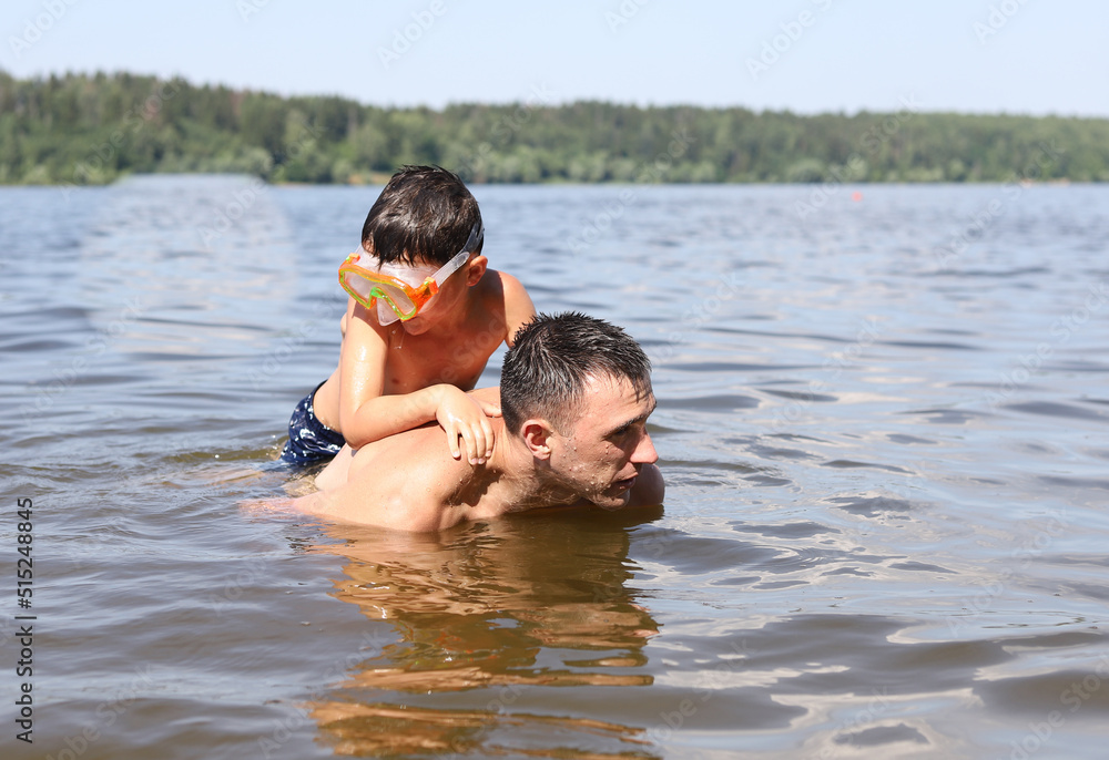 father and son swim together in a river pond father and son swim together in a river pond