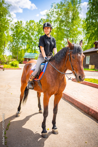 Lovely young woman wearing helmet riding her brown horse
