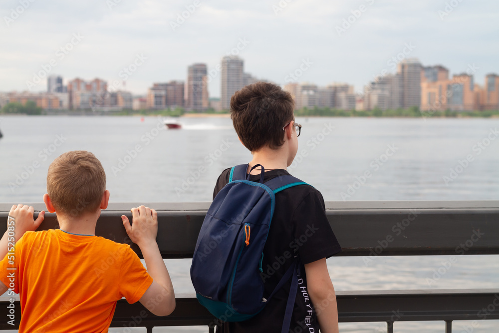 Fototapeta premium Two tourist boys admire the view of the city from the river embankment