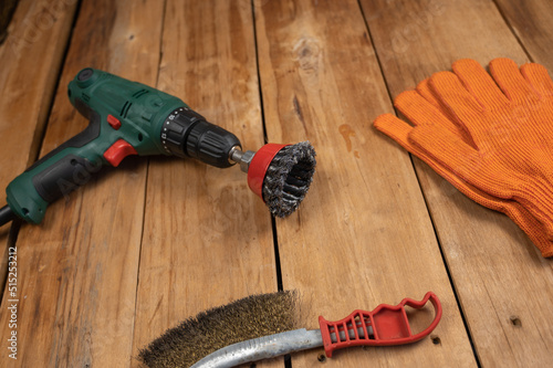 Electric drill, knot cup wire brush, metal brush and orange gloves. Hand and power tools lie on the boards. Woodworking. Top view. Selective focus.