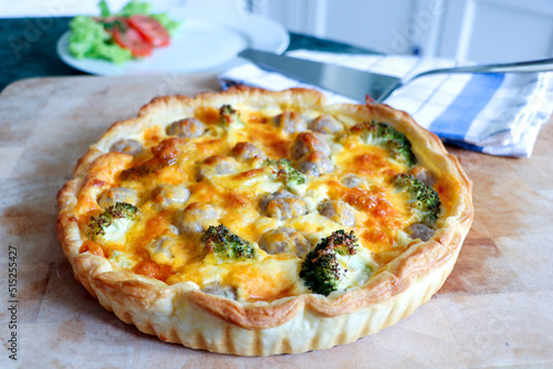 close up of quiche with cheddar cheese and broccolies served with salad and tomatoes.