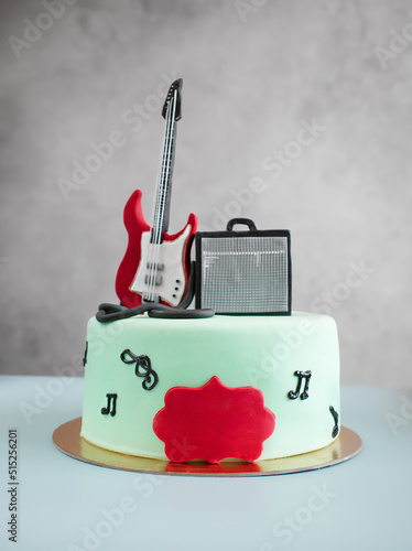 Musical themed cake with a guitar on top as a decoration. Sweet food for the musician's birthday. A gift to a creative person, a singer. Surprise for the guitarist. Top view, copy space, close up.