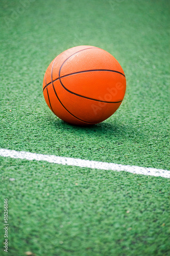 Orange basket ball lying on green playground.