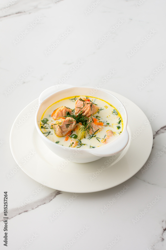 Norwegian red salmon fish soup with vegetables, herbs and cream, bowl of soup on a white marble background Norwegian red salmon fish soup with vegetables, herbs and cream, bowl of soup on a white marble background