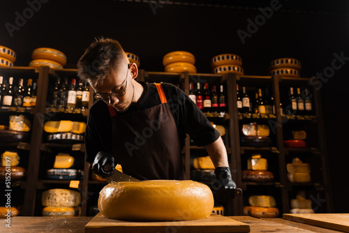 Cheese sommelier cutting yellow cheese wheel cut in half with a knife on the table. Limited maasdam cheese wheel cutting cheese in store.