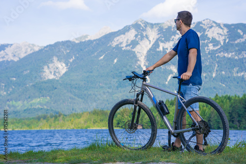 The guy sits on the grass near the bike against the background of the mountains.