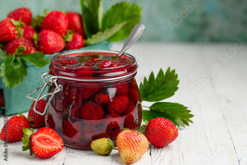 Strawberry jam with whole berries on a white wooden table. Selective focus