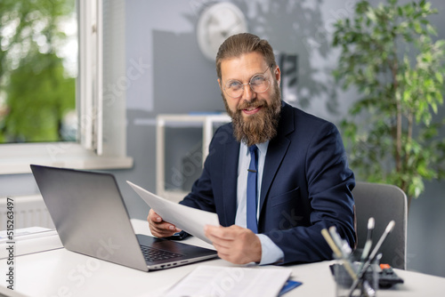Photo Smiling caucasian businessman wearing eyeglasses and stylish blue suit working with documents at office